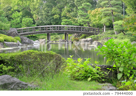 Scenery of a Japanese garden with fresh greenery and a wooden bridge reflected in the pond 79444000