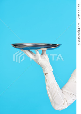 Elegant waiter's hand in white glove holding metal tray on blue background. 79445466