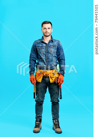 Full length portrait of handsome young male construction worker staying over blue background 79445505