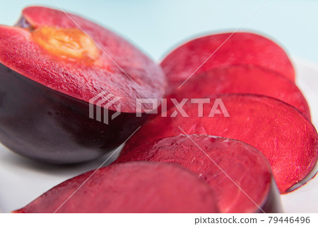 On a white saucer, a large plum, cut in half, with slices next to it. On a white saucer, a large plum, cut in half, with slices next to it. 79446496