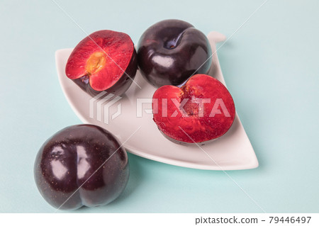 On a white saucer is a large plum, cut in half, and next to it is a whole plum. 79446497