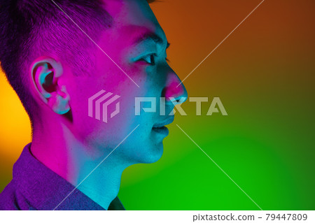 Close-up of Asian young man isolated on studio background in gradient green yellow neon light, colour filter. Concept of human emotions, facial expression. 79447809