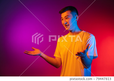 Portrait of Asian young man isolated on studio background in gradient pink purple neon light, colour filter. Concept of human emotions, facial expression. 79447813