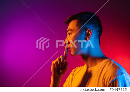 Side view. Asian young man isolated on studio background in gradient pink purple neon light, colour filter. Concept of human emotions, facial expression. 79447815