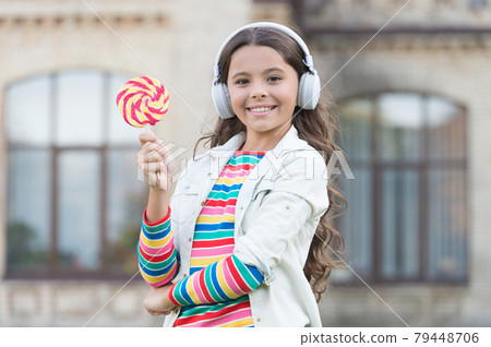 small girl eating sweet candy. happy schoolgirl in stylish hipster outfit. small girl eating sweet candy. happy schoolgirl in stylish hipster outfit. 79448706