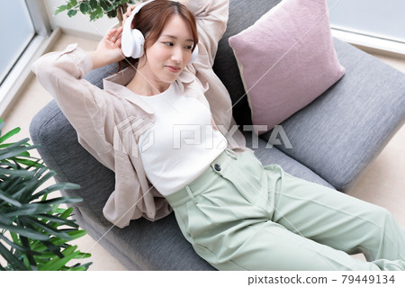 Young woman relaxing while listening to music on headphones Young woman relaxing while listening to music on headphones 79449134