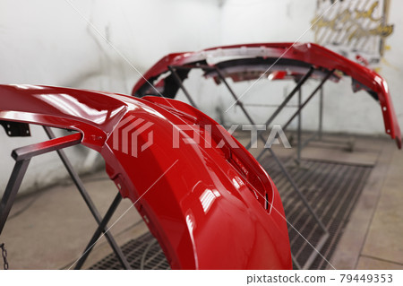 Red plastic car bumper drying after repainting in spraying booth 79449353
