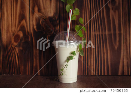 Milkshake in a plastic glass with a straw stands on a wooden background. Liquid ice cream helps you cool off in the summer heat. Drinks in a cafe or restaurant Milkshake in a plastic glass with a straw stands on a wooden background. Liquid ice cream helps you cool off in the summer heat. Drinks in a cafe or restaurant 79450565