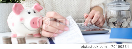 Woman holding checks for purchases in hand and counting on calculator closeup 79460284