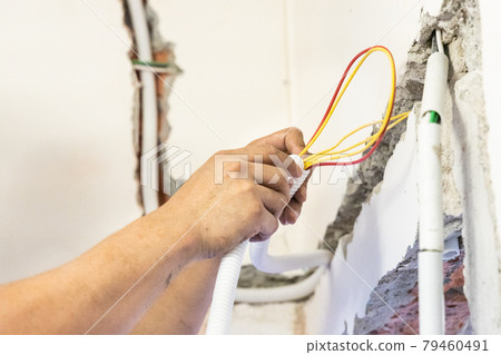 Electrician concealing electicity power wire lines within plastic tube embeded into wall 79460491