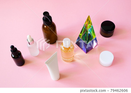 Set cosmetic beauty skin care products and glass pyramid prism on pink background, horizontal. Hydrophilic cleanser oil, serums, body lotion, moisturizer creams. 79462606