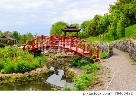 Red bridge and gazebo by a pond in Japanese garden 79463488