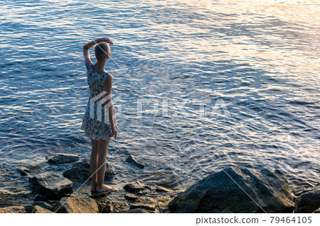 girl teenager in a dress stands on the seashore, looking into the distance 79464105