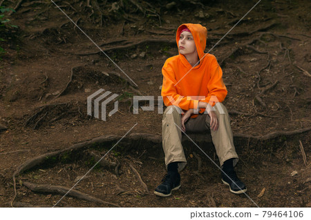 sad teenager in a hoodie sits on a natural background sad teenager in a hoodie sits on a natural background 79464106
