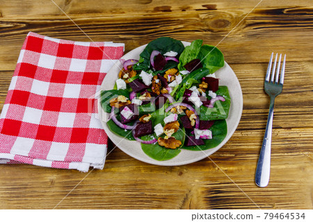 Tasty spinach salad with boiled beetroot, feta cheese, walnut and red onion on wooden table. Healthy vegetarian food 79464534