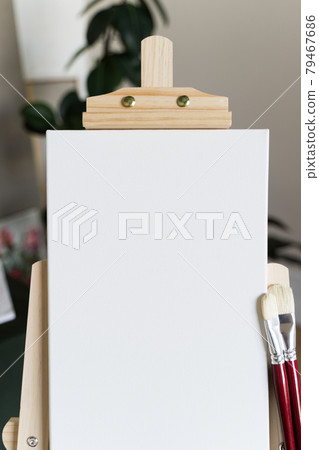 Creative studio. Empty white canvas on a wooden easel and red brushes Creative studio. Empty white canvas on a wooden easel and red brushes 79467686