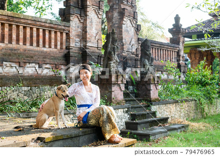 A woman and a dog in traditional costumes (Kebaya) at a traditional temple in Bali 79476965
