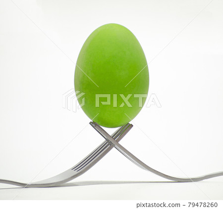 A green chicken egg is placed on the tip of a cutlery on a white background. A green chicken egg is placed on the tip of a cutlery on a white background. 79478260