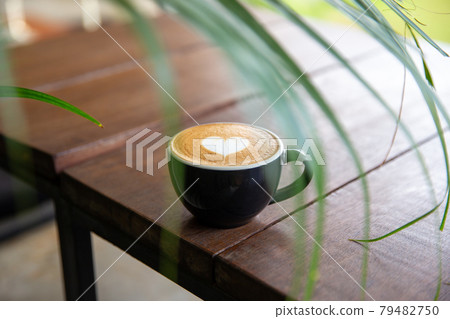 Black cup of cappuccino with latte art of heart shape on saucer on concrete background. Black cup of cappuccino with latte art of heart shape on saucer on concrete background. 79482750