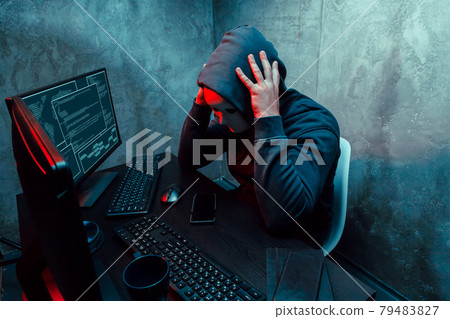 Anonymous internet hacker with mask sitting at the table and using computer Anonymous internet hacker with mask sitting at the table and using computer 79483827