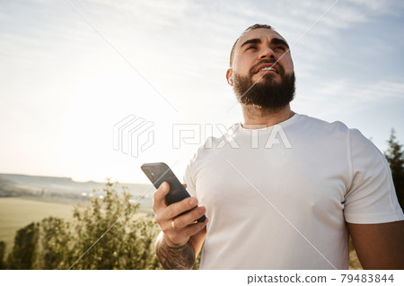 Young male using cell telephone while having a walk in countryside Young male using cell telephone while having a walk in countryside 79483844