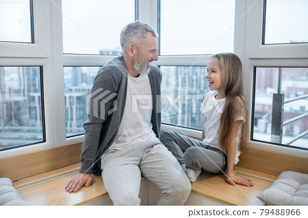 A dad sitting at the window with his daughter 79488966
