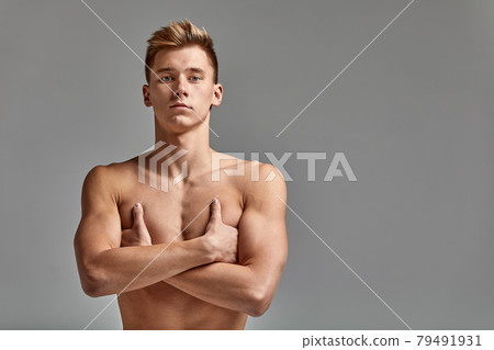 A male swimmer stands with crossed arms, on a gray background, challenging, spears space 79491931
