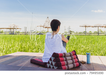 Woman sit on wooden floor looking at cell phone with nature landscape view. 79495890
