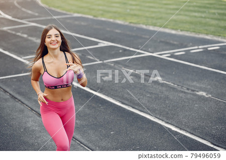 Sports girl in a pink uniform runs at the stadium Sports girl in a pink uniform runs at the stadium 79496059