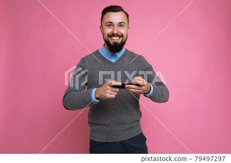 Shot of happy joyful handsome young brunette unshaven man with beard wearing everyday grey sweater Shot of happy joyful handsome young brunette unshaven man with beard wearing everyday grey sweater 79497297