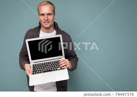 Close-up portrait of handsome blonde man holding computer laptop looking at camera isolated over Close-up portrait of handsome blonde man holding computer laptop looking at camera isolated over 79497378