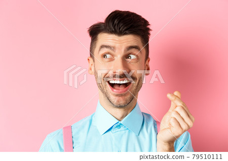 Valentines day concept. Romantic guy showing finger heart and looking left, smiling happy, standing on pink background dreamy Valentines day concept. Romantic guy showing finger heart and looking left, smiling happy, standing on pink background dreamy 79510111