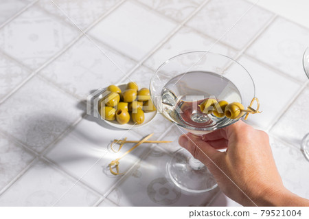 Hand holds glass of Martini cocktail with olives. Alcoholic classic drink with ice deep shadows bright sunlight Hand holds glass of Martini cocktail with olives. Alcoholic classic drink with ice deep shadows bright sunlight 79521004