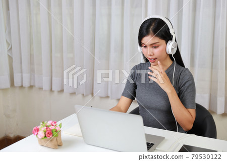Young smart and active asian female student sitting at table with headset, using computer and taking note for studying online with happy smiling face (new normal concept) Young smart and active asian female student sitting at table with headset, using computer and taking note for studying online with happy smiling face (new normal concept) 79530122
