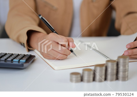 Smart and active asian businesswoman hands writing something on notebook with saving growth on stacking coin on table, meaning of earning money or investment or tax for business advertising concept Smart and active asian businesswoman hands writing something on notebook with saving growth on stacking coin on table, meaning of earning money or investment or tax for business advertising concept 79530124