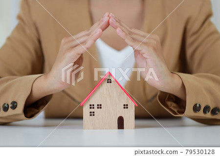 Young active business woman hands in casual dress sitting and protecting house model on white table. Property insurance and security concept Young active business woman hands in casual dress sitting and protecting house model on white table. Property insurance and security concept 79530128