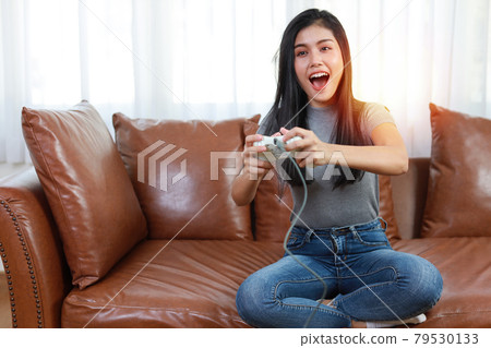 VDO game console station concept. active asian woman sitting on sofa, holding joystick and playing exciting game. Cute girl looked excited with game controller console 79530133