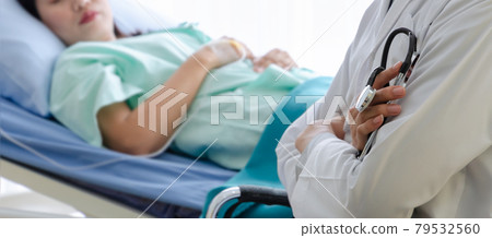 Doctor holding stethoscope and sitting in front of sick woman patient bed in hospital room. 79532560