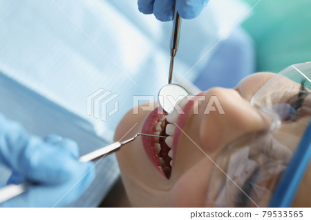 Dentist in protective gloves examining teeth of female patient using metal instruments in clinic closeup 79533565