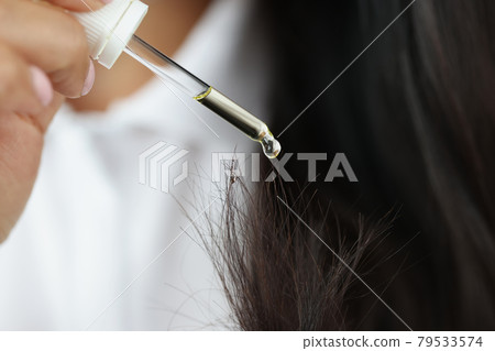 Woman dripping yellow oil from pipette on split ends of hair closeup Woman dripping yellow oil from pipette on split ends of hair closeup 79533574