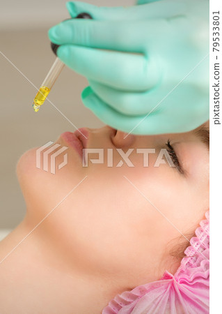 Close up of beautician holding pipette and applying oil serum drop on the face of a young woman in spa salon. 79533801