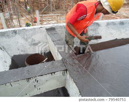 SELANGOR, MALAYSIA -SEPTEMBER 16, 2014: Construction worker apply layers of bituminous waterproofing at the building roof slab surface. SELANGOR, MALAYSIA -SEPTEMBER 16, 2014: Construction worker apply layers of bituminous waterproofing at the building roof slab surface. 79540751