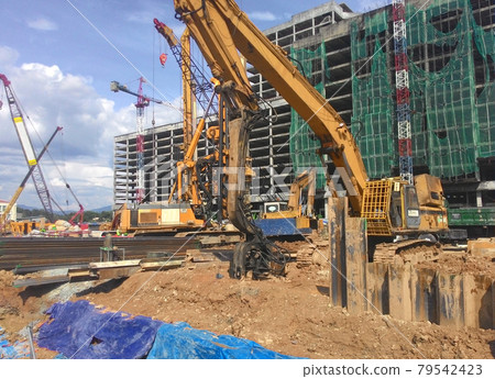 SELANGOR, MALAYSIA -APRIL 15, 2016: Sheet pile cofferdam driven machine at the construction site. The machine drove the sheet pile to the earth using vibrated hydraulic arm. Workers control. SELANGOR, MALAYSIA -APRIL 15, 2016: Sheet pile cofferdam driven machine at the construction site. The machine drove the sheet pile to the earth using vibrated hydraulic arm. Workers control. 79542423
