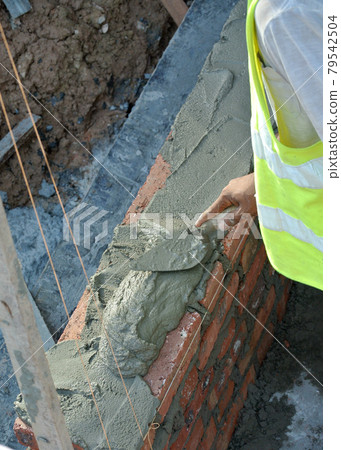 JASIN, MALAYSIA -SEPTEMBER 09, 2016: Brick walling joint and workmanship under construction at the construction site. Clay brick was attached together using cement mortar. JASIN, MALAYSIA -SEPTEMBER 09, 2016: Brick walling joint and workmanship under construction at the construction site. Clay brick was attached together using cement mortar. 79542504