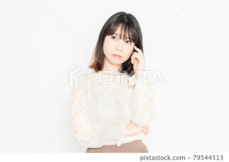 A young woman in a lace blouse, worried, standing in front of a white background 79544513