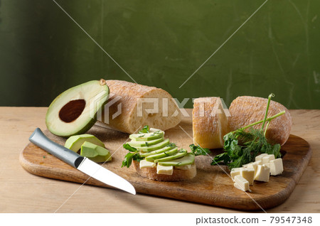 Making sandwiches with herbs and avocado. White bread and cheese slices. Cooking sandwiches on the board. Green background. 79547348