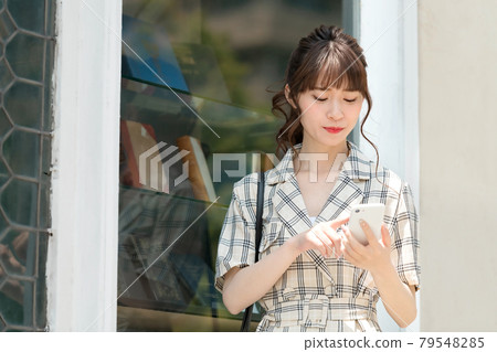 A young business woman in plain clothes who operates a smartphone outdoors A young business woman in plain clothes who operates a smartphone outdoors 79548285