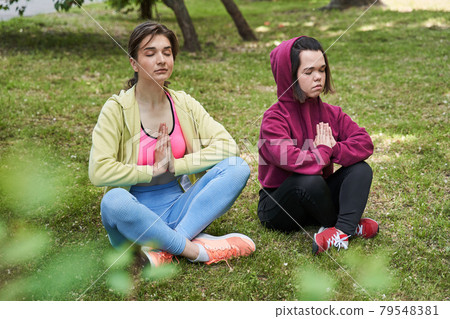 Young girls keeping prayer gesture while meditating at the park Young girls keeping prayer gesture while meditating at the park 79548381