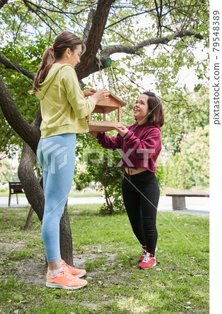 Midget woman adjusting birds feeder at the tree with her best friend Midget woman adjusting birds feeder at the tree with her best friend 79548389