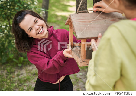 Woman adjusting birds feeder at the tree and looking at her best friend 79548395
